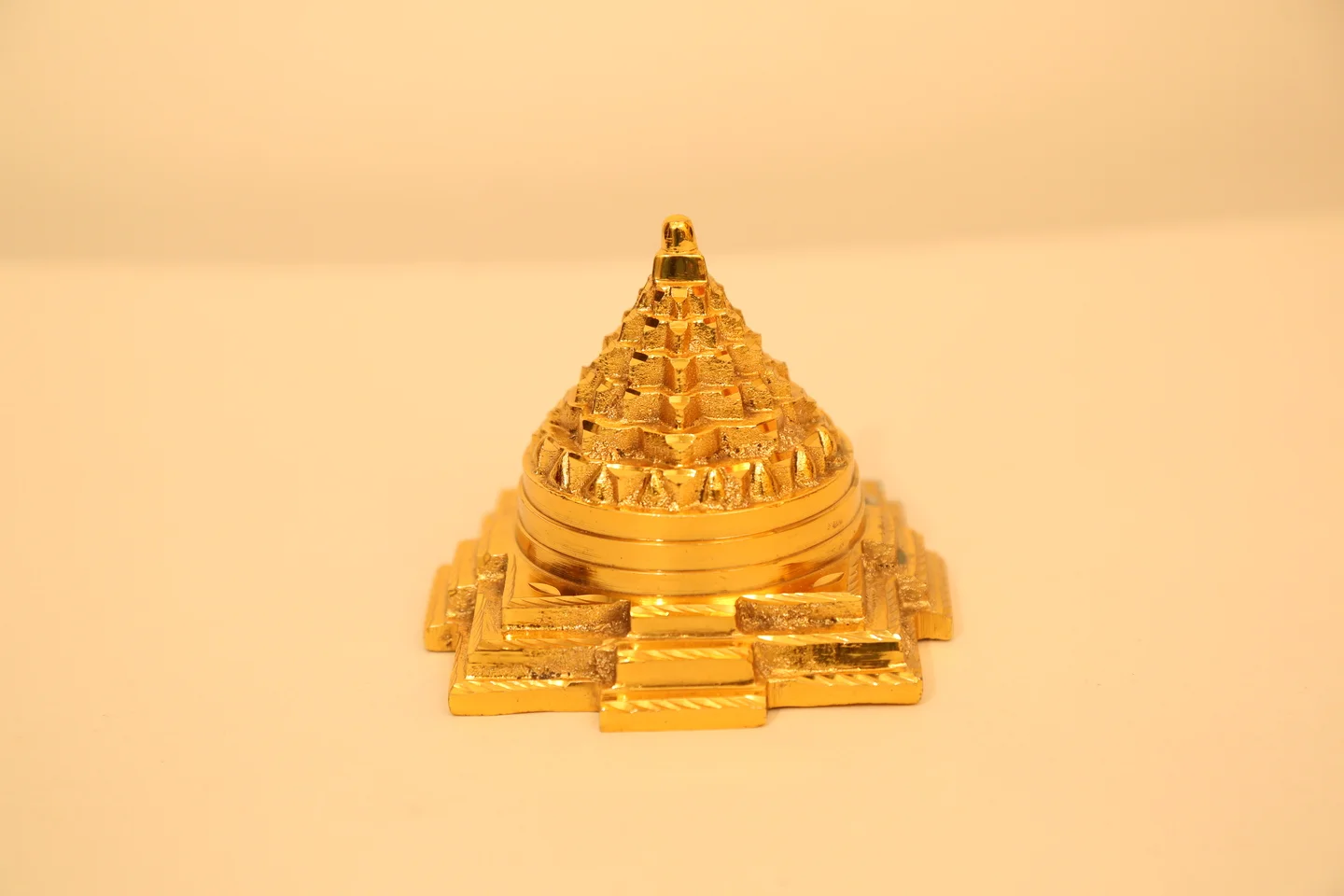 Golden Sri Yantra pyramid sculpture placed on a light background for Vastu and spiritual energy