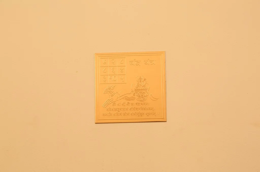 Gold Vastu yantra plate with sacred symbols and numbers mounted on a beige wall